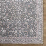 Close-up of the Anando Washable Area Rug. Features a traditional floral pattern in cream, pale pink, and green on a gray background. Corner