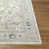 Close-up of the Ayzize Ivory Area Rug showing its traditional pattern and colors on a wood floor. Front