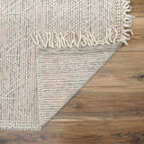 Close-up of Ramsbury Wool Area Rug showing ivory, black geometric pattern, woven texture, and fringe detail on wood floor. Fold