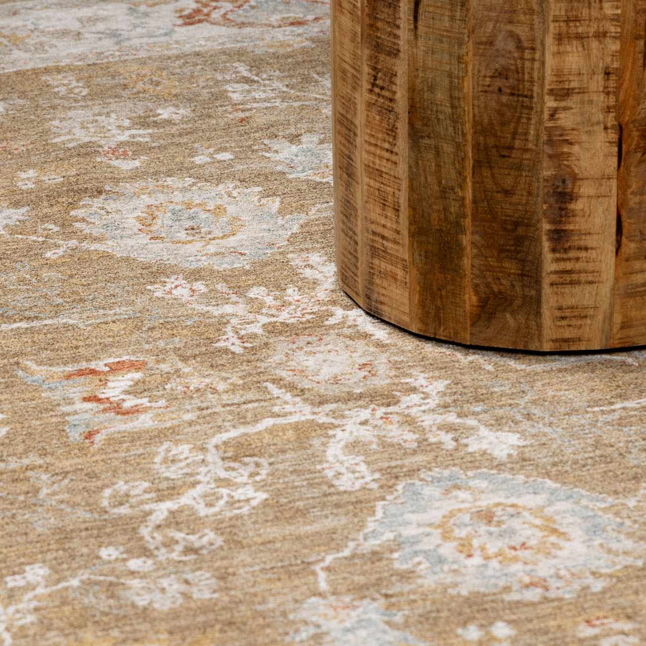 Close-up of the brown Rangeville Thick Luxe Statement Rug with a traditional floral pattern and a rustic wood table leg. Styleshot