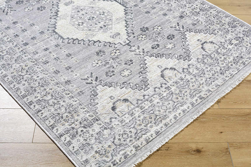 Close-up of the Aoibhe Area Rug. Machine woven polyester rug in ivory, medium gray, and slate gray with a traditional pattern. Corner