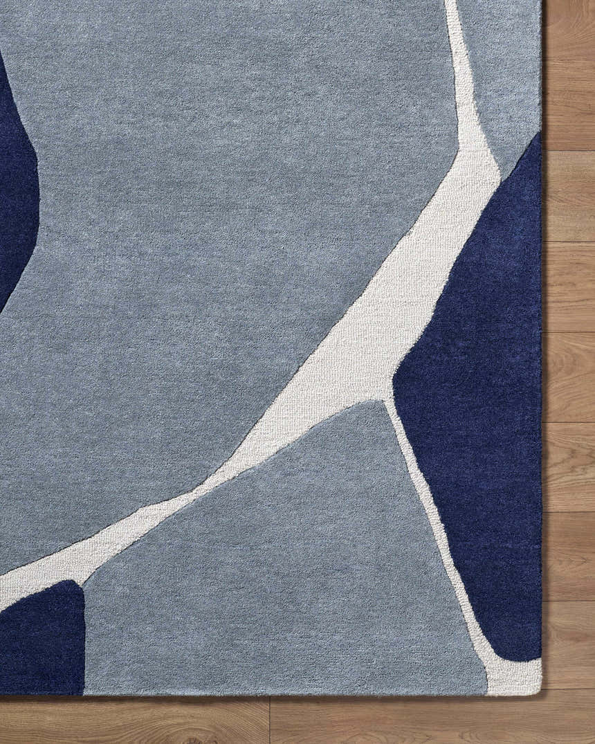 Close-up of the Robbins Modern Blue Wool Rug featuring a geometric design in blue, light slate, and navy on a wood floor. Corner