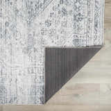 Close-up of the Barny Gray Blue Washable Rug showing its traditional, faded charcoal and off-white pattern and gray backing. Fold
