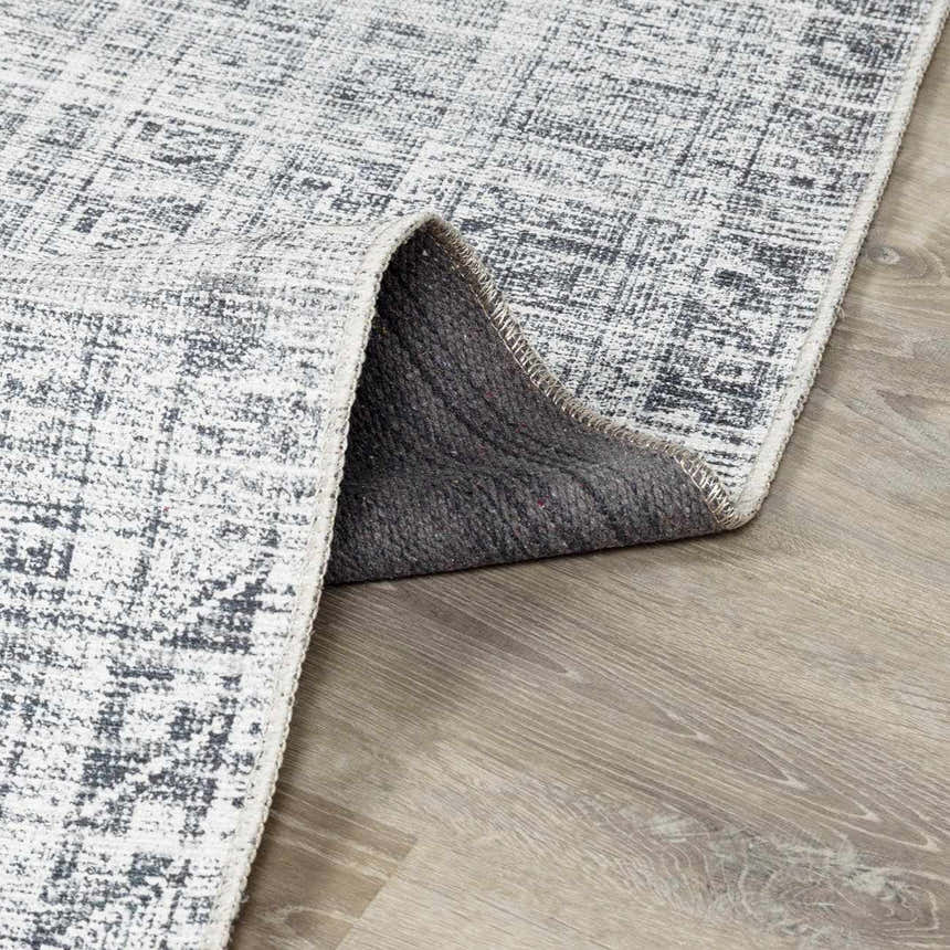 Close-up of the Barny Gray Blue Washable Rug showing its charcoal and off-white distressed pattern and gray backing. Fold