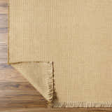 Close-up of the Kimi Becki Owens x LIVABLISS rug. Light brown jute with woven texture and fringed edge on wood floor. Fold