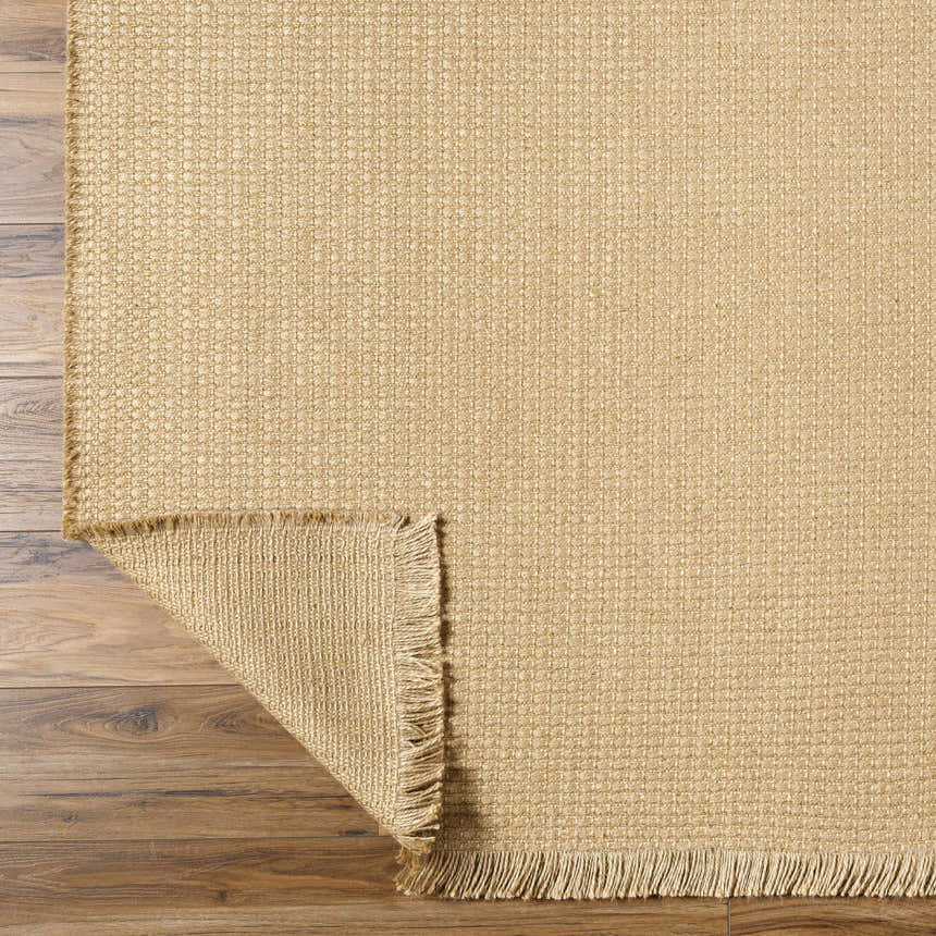 Close-up of the Kimi Becki Owens x LIVABLISS rug. Light brown jute with woven texture and fringed edge on wood floor. Fold