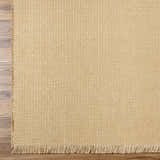 Close-up of the light brown Kimi Machine Woven Becki Owens x LIVABLISS rug showing jute texture and fringe detail. Corner
