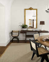 Farmhouse dining room with Kimi Machine Woven Becki Owens rug, wood table, chairs, and gold mirror. Gray, tan, and light brown tones. Styleshot