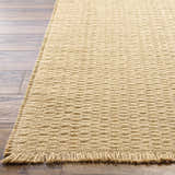 Close-up of Kimi Machine Woven Becki Owens x LIVABLISS rug showing light brown jute texture and fringe detail on wood floor. Front