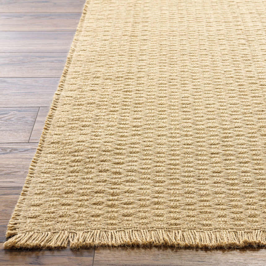 Close-up of Kimi Machine Woven Becki Owens x LIVABLISS rug showing light brown jute texture and fringe detail on wood floor. Front