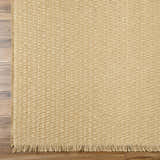 Close-up of the light brown Kimi Becki Owens x LIVABLISS rug showing jute texture and fringe detail on wood floor. Corner