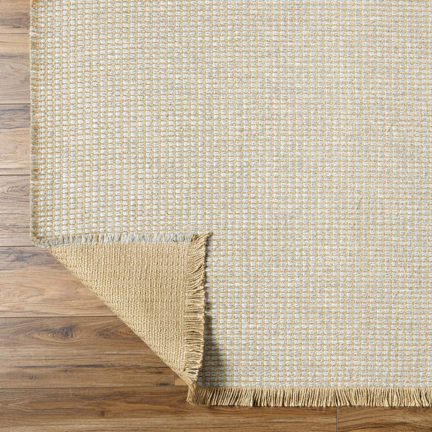Close-up of Kimi Machine Woven Becki Owens x LIVABLISS rug. Gray and light brown jute texture with fringe detail. Fold