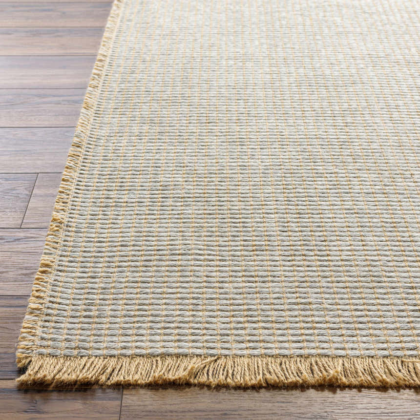 Close-up of Kimi Becki Owens x LIVABLISS rug. Jute texture in gray and light brown with fringe detail on wood floor. Front