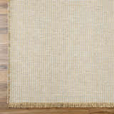 Close-up of Kimi Machine Woven Becki Owens x LIVABLISS rug. Gray and light brown jute texture with fringe detail. Corner