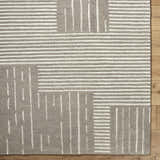 Close-up of Akuji Area Rug. Gray wool rug with a contemporary pattern of white stripes and rectangles on wood floor. Corner