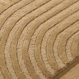 Close-up of the hand-tufted Whan Camel Area Rug. The 100% wool rug features a contemporary, curved line design. Texture