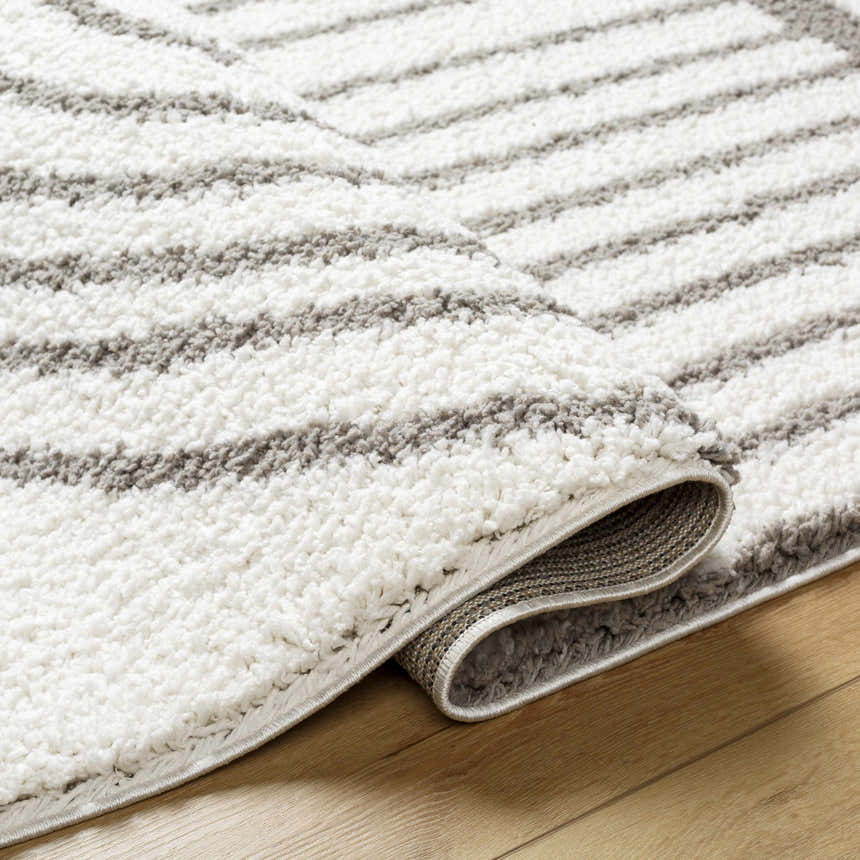 Close-up of the Jola Taupe Area Rug, showcasing its plush texture and geometric pattern in beige, bone, and gray tones. Fold
