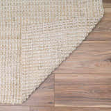 Close-up of the hand-woven Ambel Cream Jute Rug showing its bone color and natural jute texture on wood flooring. Fold