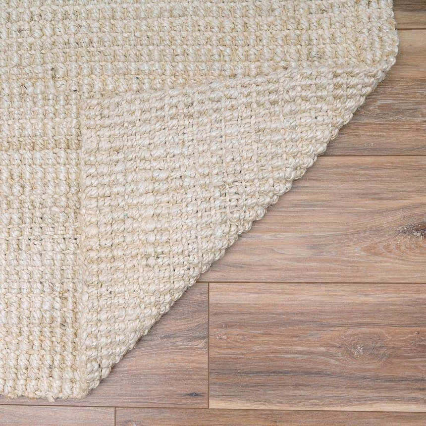 Close-up of the hand-woven Ambel Cream Jute Rug showing its bone color and natural jute texture on wood flooring. Fold