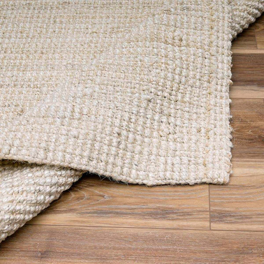 Close-up of the hand-woven Ambel Cream Jute Rug showing its bone color and natural fiber texture on a wood floor. Fold