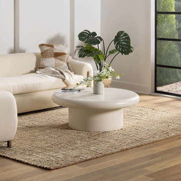 Living room scene with a neutral sofa, round coffee table, and the Ambel Tan Camel Jute Area Rug adding texture and warmth. Roomscene-Rectangle
