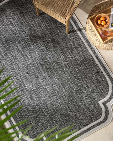 Outdoor patio scene with a black and cream Arnola Black Outdoor Rug, wicker chair, and side table. Roomscene-Rectangle