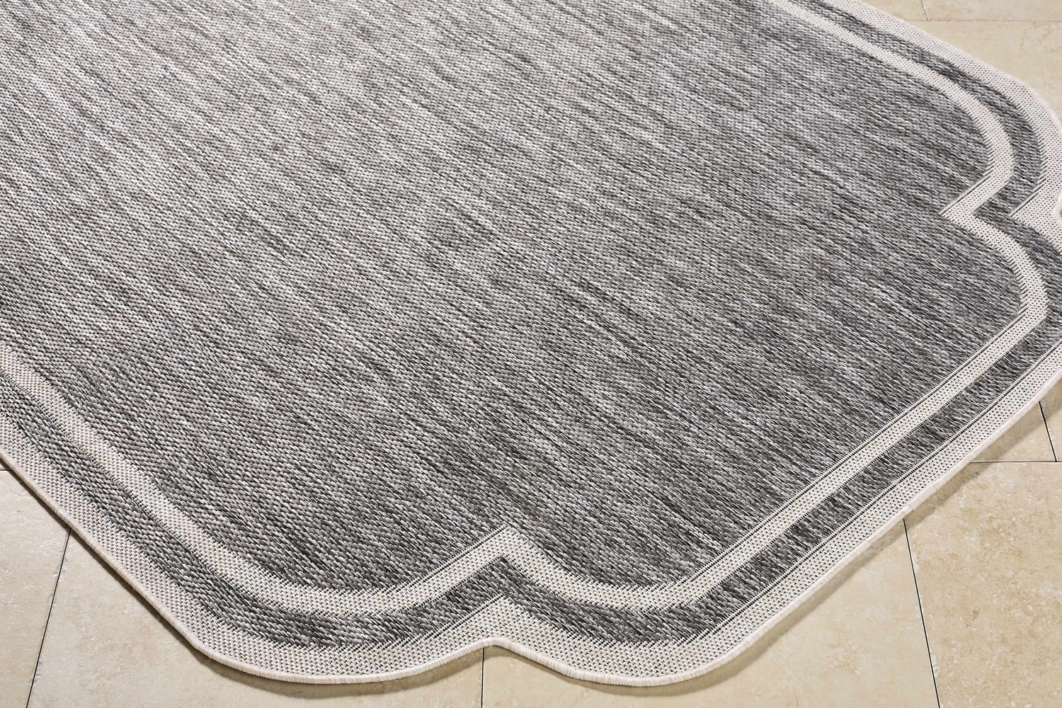 Close-up of Arnola Gray Outdoor Rug showing charcoal, cream, and gray woven texture and farmhouse style border. Corner