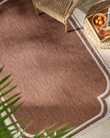 Outdoor patio scene with a brown Arnola Brown Outdoor Rug, wicker chair and table. Roomscene-Rectangle