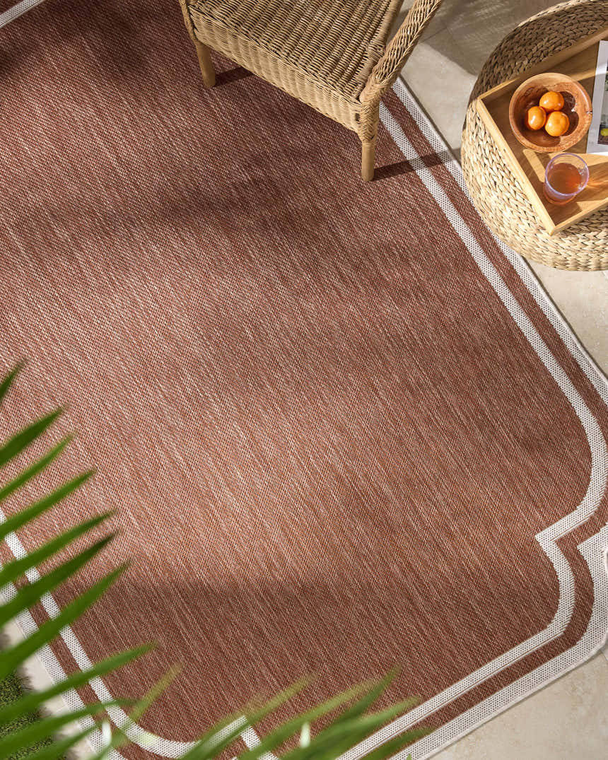 Outdoor patio scene with a brown Arnola Brown Outdoor Rug, wicker chair and table. Roomscene-Rectangle