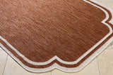 Close-up of Arnola Brown Outdoor Rug showing brown woven texture and cream geometric border on a tile floor. Corner
