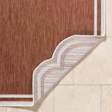 Close-up of the Arnola Brown Outdoor Rug showing the weave, brown color, and cream border on tile flooring. Fold