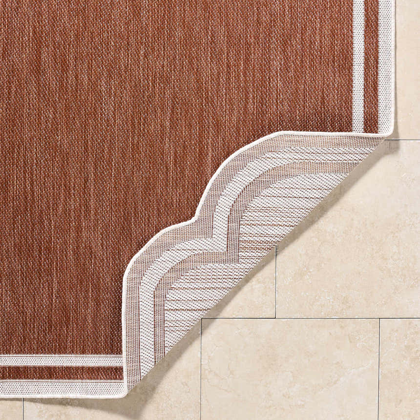 Close-up of the Arnola Brown Outdoor Rug showing the weave, brown color, and cream border on tile flooring. Fold