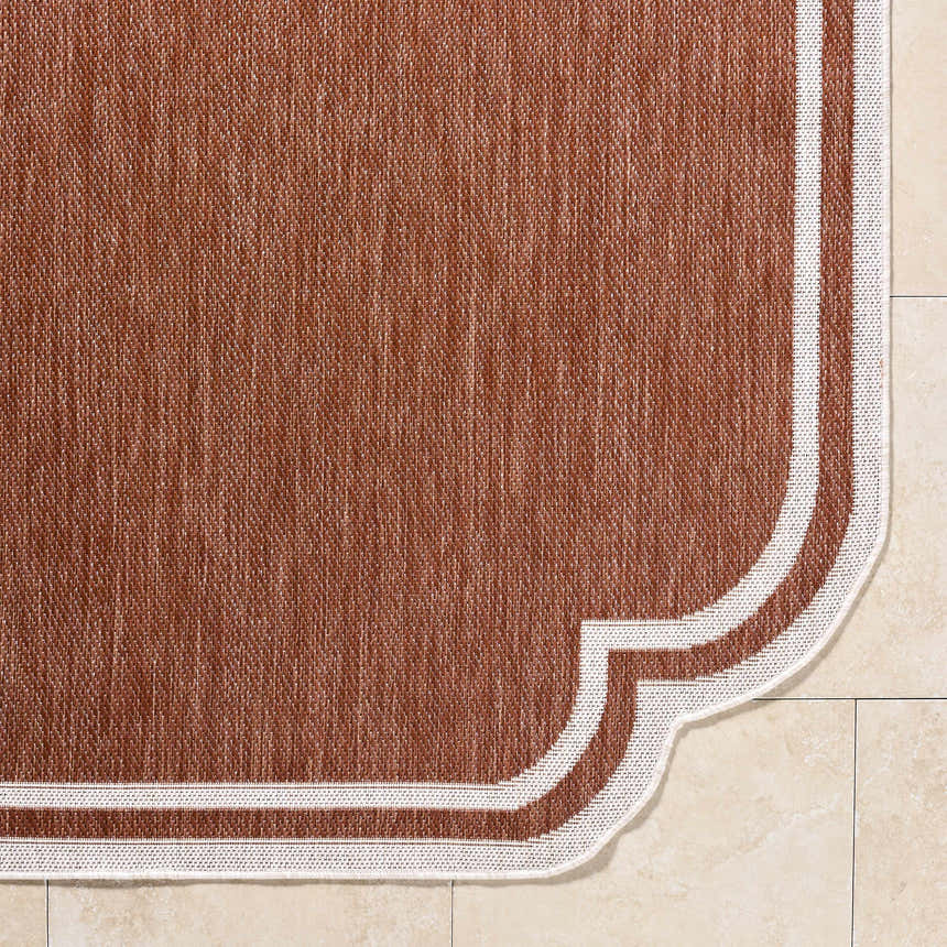 Close-up of the Arnola Brown Outdoor Rug showing the woven texture and cream border detail. Corner