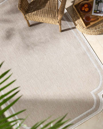 Tan patio scene with a wicker chair and the Arnola Tan Outdoor Rug. Roomscene-Rectangle