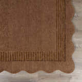 Close-up of the hand-tufted Gurib Border Wool Area Rug. Features a wavy edge and striped border in neutral brown tones. Corner