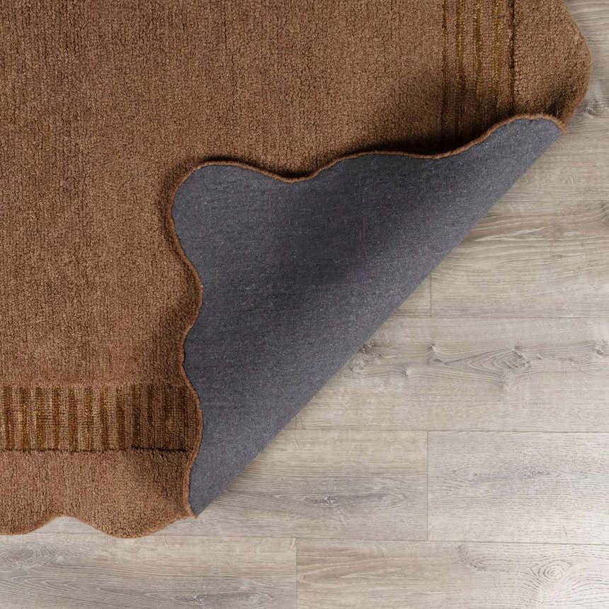 Close-up of the brown Gurib Border Modern Hand Tufted Wool Area Rug showing texture, backing, and scalloped edge. Fold