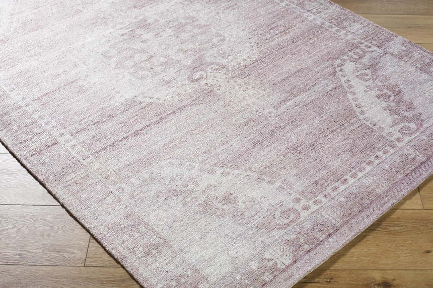 Close-up of the Alafin Area Rug. Hand-tufted polyester rug in blush, cream, dusty rose, and mauve on wood floor. Corner