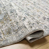 Close-up of the Chaka Textured Rug. Features a contemporary geometric pattern in off-white, gray, blue, and mustard. Fold