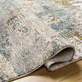 Close-up of Chaya Textured Abstract Rug. Features dusty sage, ink blue, light gray, and mustard hues. Machine woven texture. Fold