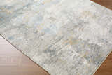 Close-up of the Gryta Textured Rug with Fringes. Features gray, light blue, and gold tones on a textured, contemporary design. Corner