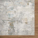 Close-up of the Gryta Textured Rug with Fringes. Features a gray, white, blue, and gold abstract pattern. Contemporary style. Corner