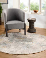 Living room scene with gray chair and round Haydn Rock Pattern Rug in gray, brown, and cream tones. Roomscene-Round