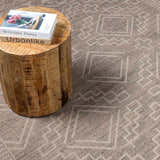 Close-up of Halle Beige Washable Area Rug with geometric pattern and a wood side table holding books. Styleshot