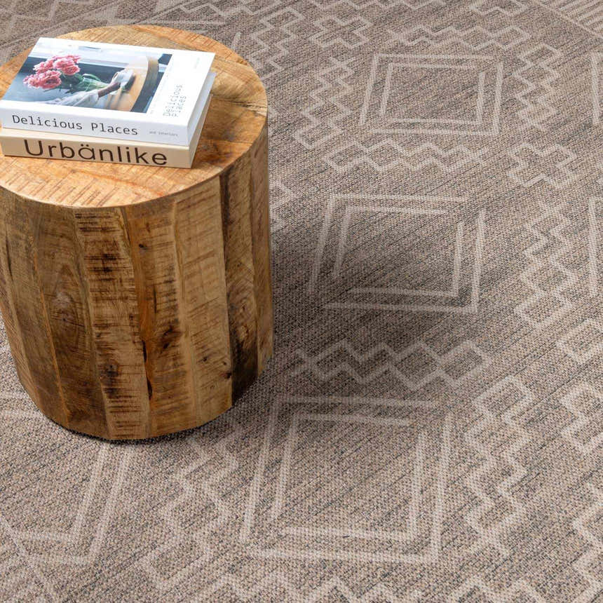 Close-up of Halle Beige Washable Area Rug with geometric pattern and a wood side table holding books. Styleshot