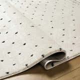 Close-up of Julie Area Rug. Beige rug with black polka dot pattern and soft texture. Rolled edge detail. Fold