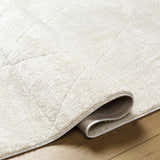 Close-up of the ivory Keone Area Rug showing its plush texture and geometric pattern on a wood floor. Fold