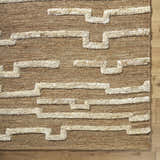 Close-up of the hand-woven Miya Area Rug. Jute rug in beige and tan with a geometric, ivory-colored pattern. Farmhouse style. Corner