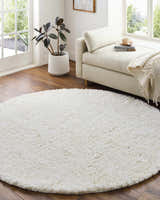 Sunlit room with a round Siari Solid Cream Plush Rug, chaise lounge, and potted plant, creating a cozy, inviting space. Roomscene-Round