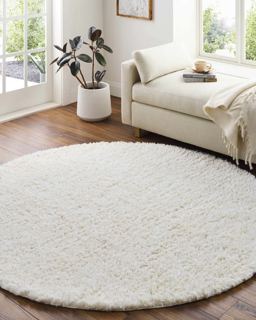 Sunlit room with a round Siari Solid Cream Plush Rug, chaise lounge, and potted plant, creating a cozy, inviting space. Roomscene-Round