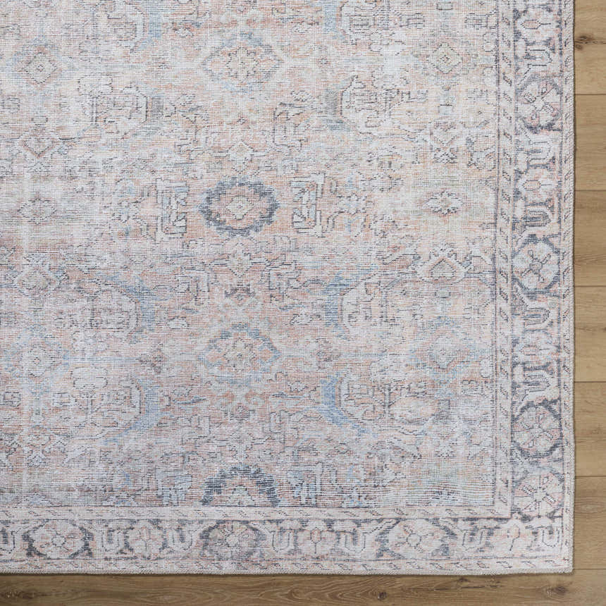 Close-up of the Giona Washable Area Rug. Machine woven with a vintage Persian pattern in blue, charcoal, and pastel red. Corner